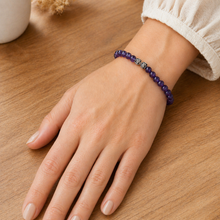Load image into Gallery viewer, Woman wearing deep purple crystal bracelet on wrist over wooden table in soft indoor light