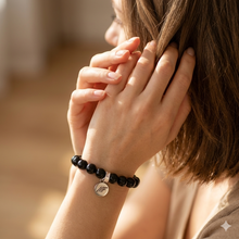 Load image into Gallery viewer, MysticFlavia black obsidian bracelet 8mm with silver brand charm worn on wrist with hands clasped near face