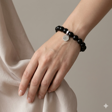 Load image into Gallery viewer, Black obsidian flat silver bead bracelet worn on wrist against beige silk fabric background