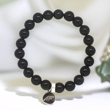 Load image into Gallery viewer, Black obsidian flat silver bead bracelet 8mm on white fabric surface with round brand charm pendant