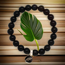 Load image into Gallery viewer, MysticFlavia black tourmaline bracelet with silver charm, flat lay on wooden surface with green leaf