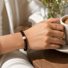 Load image into Gallery viewer, Female model wearing Garnet Birthstone Infinity Silver Bead Bracelet 8mm while holding a coffee cup in a cozy lifestyle setting