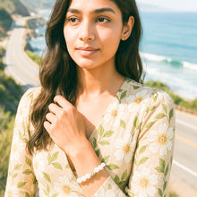 Load image into Gallery viewer, MysticFlavia selenite bracelet with milky white beads and silver infinity bead worn by woman in floral outfit, outdoor coastal lifestyle shot
