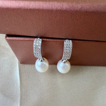 Load image into Gallery viewer, White pearl drop earrings with textured silver rectangular tops arranged on a red jewelry box.