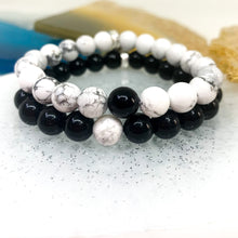 Load image into Gallery viewer, Black Obsidian and White Howlite couple bracelets close-up showing beads on glittered surface