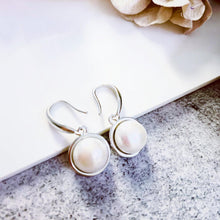 Load image into Gallery viewer, White pearl silver drop earrings on a textured surface.