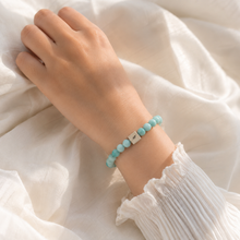 Load image into Gallery viewer, Natural amazonite infinity bracelet with teal beads and silver brand tag worn on wrist, soft white fabric lifestyle shot

