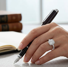 Load image into Gallery viewer, Elegant 925 sterling silver ring with a cushion-cut gemstone and halo setting worn on a woman’s hand while writing.
