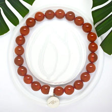Load image into Gallery viewer, Polished Carnelian bead bracelet with silver charm, displayed on white surface with green leaf
