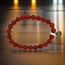 Load image into Gallery viewer, Natural Carnelian stone bead bracelet with silver logo charm, dramatic golden light studio shot
