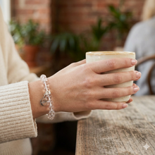 Load image into Gallery viewer, MysticFlavia clear quartz flat silver bead bracelet worn on wrist holding a coffee cup, café setting
