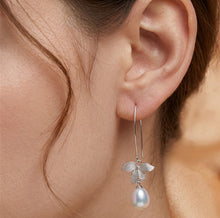 Load image into Gallery viewer, Silver floral pearl dangling earring worn on a model’s ear, close-up view
