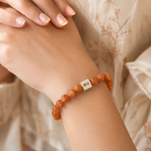 Load image into Gallery viewer, Natural sunstone infinity bracelet with golden-brown beads and silver infinity charm worn on wrist, soft fabric lifestyle shot


