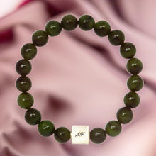 Load image into Gallery viewer, Jade infinity bracelet close-up on fabric background showing silver MF charm

