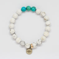 Turquoise and howlite flat silver bead bracelet with white marbled beads, three teal turquoise beads on top and round silver brand charm, white background
