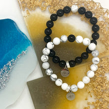 Load image into Gallery viewer, Black Obsidian and White Howlite couple bracelets on blue and gold background with silver charms

