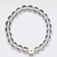 MysticFlavia clear quartz bracelet with 925 sterling silver cube bead engraved with MF initials, flat lay on white