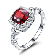 Red gemstone silver ring with a halo of sparkling stones in an elegant cushion-cut design.