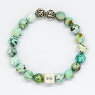 Turquoise infinity round silver bracelet with natural green-teal speckled beads, two carved silver beads on top and square infinity charm, white background
