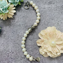 Load image into Gallery viewer, White Pearl Silver Toggle Clasp Bracelet styled on a stone surface with decorative flowers
