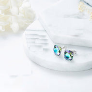 Swarovski crystal stud earrings in iridescent blue-green, close-up on white fabric background.